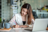 Beautiful asian businesswoman or financial manager working in modern office on laptop. Businesswoman working on laptop and taking note while sitting at the table in office.