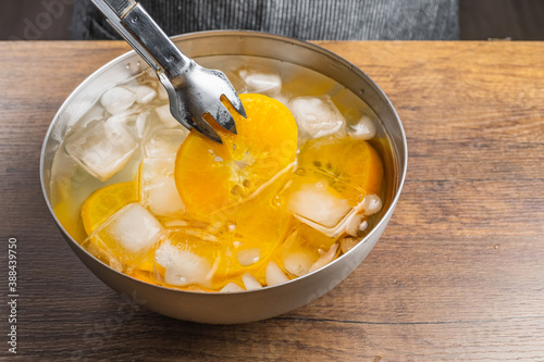 Putting cooked orange slices with a tongs in ice water to cool down after cooking in hot water.