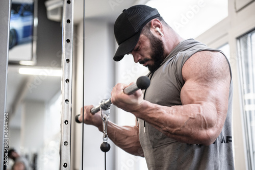 strong bearded man with huge muscle lifting heavy weitht in sport gym during training workout leisure activity listening music in earpieces