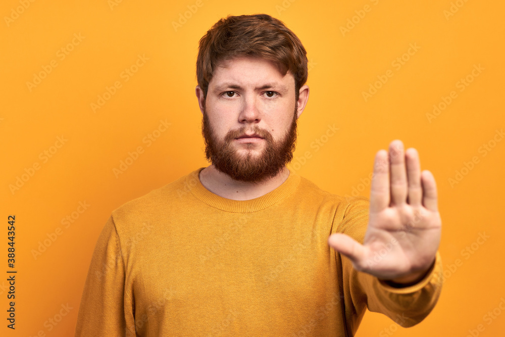 a young bearded man looking serious, angry and displeased forbidding to enter or saying stop, forbidding with his hand on a yellow background a young bearded man looking serious, angry and displeased forbidding to enter or saying stop, forbidding with his hand on a yellow background