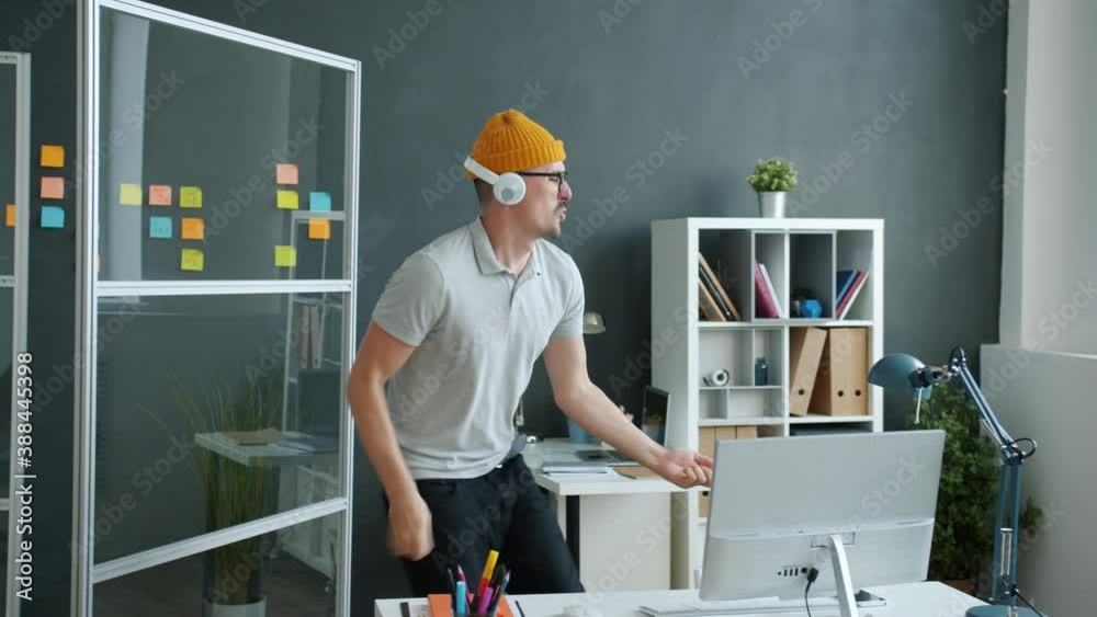 Crazy young man hipster is enjoying music through headphones dancing and having fun in office alone. Workplace and relaxation activities concept.