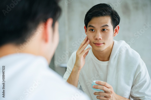 Young man apply facial cream lotion at mirror in bathroom.
