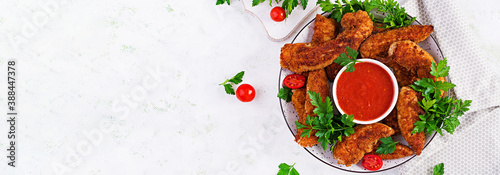 Breaded mini chicken fillets served with tomato sauce. American food. Chicken nuggets with parsley. Top view, banner, copy space