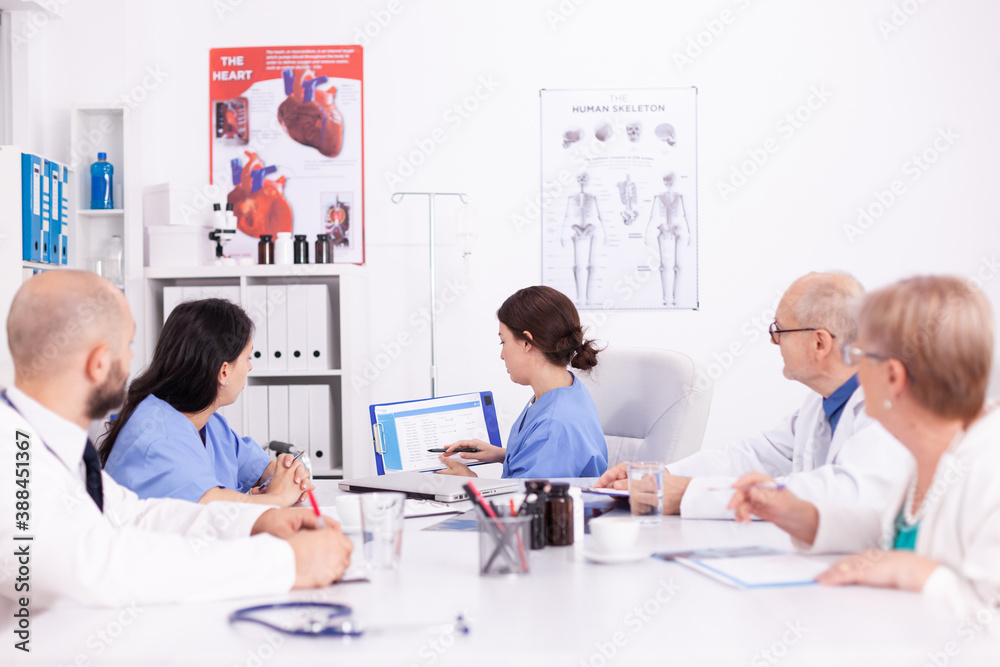 Female nurse holding clipboard explaining her diagnosis in front of medicine experts during seminar. Clinic therapist talking with colleagues about disease, medicine professional Female nurse holding clipboard explaining her diagnosis in front of medicine experts during seminar. Clinic therapist talking with colleagues about disease, medicine professional