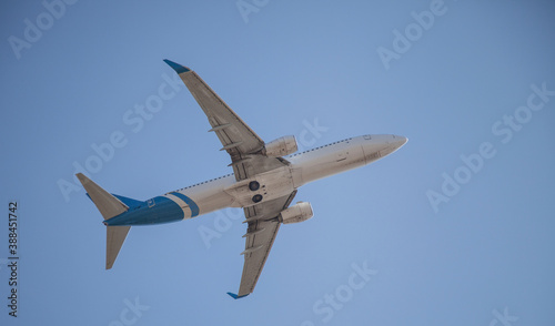 White plane flies in the sky. Bottom view. Takeoff and landing. Arrival and departure. Passenger plane isolated on blue background. Passenger airplane. Travel by air transport. Copy space. Flying.