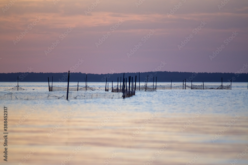 Krajobraz morski z rozstawionymi sieciami połowowymi na tle zachodzącego słońca