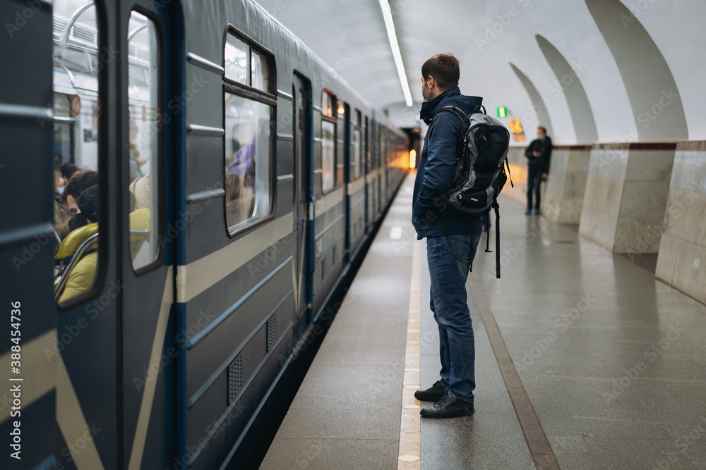 Fototapeta premium caucasian man wearing medicine mask going to get in subway car on platform of underground station in saint petersburg, Russia. Image with selective focus