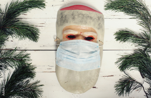 Foto Old vintage retro papier mache mask of Santa Claus with mask on face because of coronavirus pandemic restrictions on white wooden background