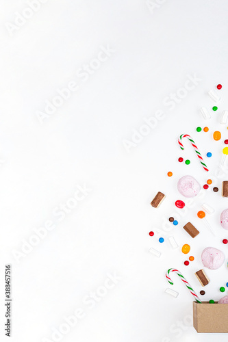 Box with various colored sweets on a white background. Festive concept. Lollipops, caramel, candy canes, marshmallows, chocolate top view