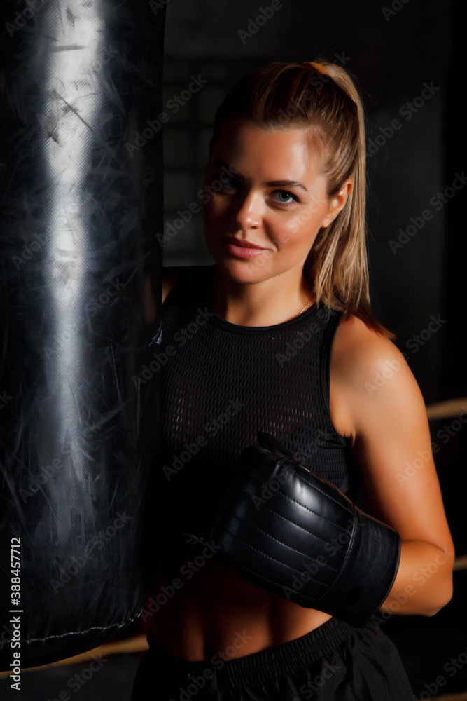 Pretty young female boxer is standing in ring at punching bag in an old gym, her hands in Boxing gloves. Woman in box training. Concept of healthy lifestyle, sports and exercise in gym. Copy space