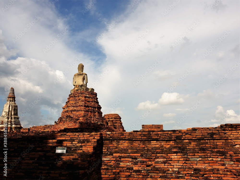 Ancient Buddhist monk statue on red brick foundation facing the sky from a historical landmark temple in Thailand