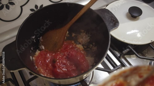 Adding fresh tomato sauce into cooking hot pot on a gas stove. photo