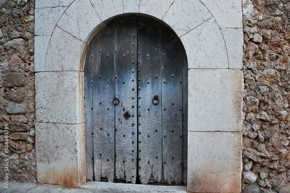 ancient wooden door arch shape with metal round handles is entrance of old stone castle of house in European town.  Historical object on european streets