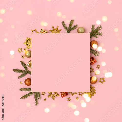 Square pink paper card mockup with frame made of Christmas decorations and fir branches. Shiny composition with golen bokeh. photo