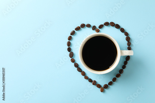 Heart made of coffee beans and cup of coffee on blue background