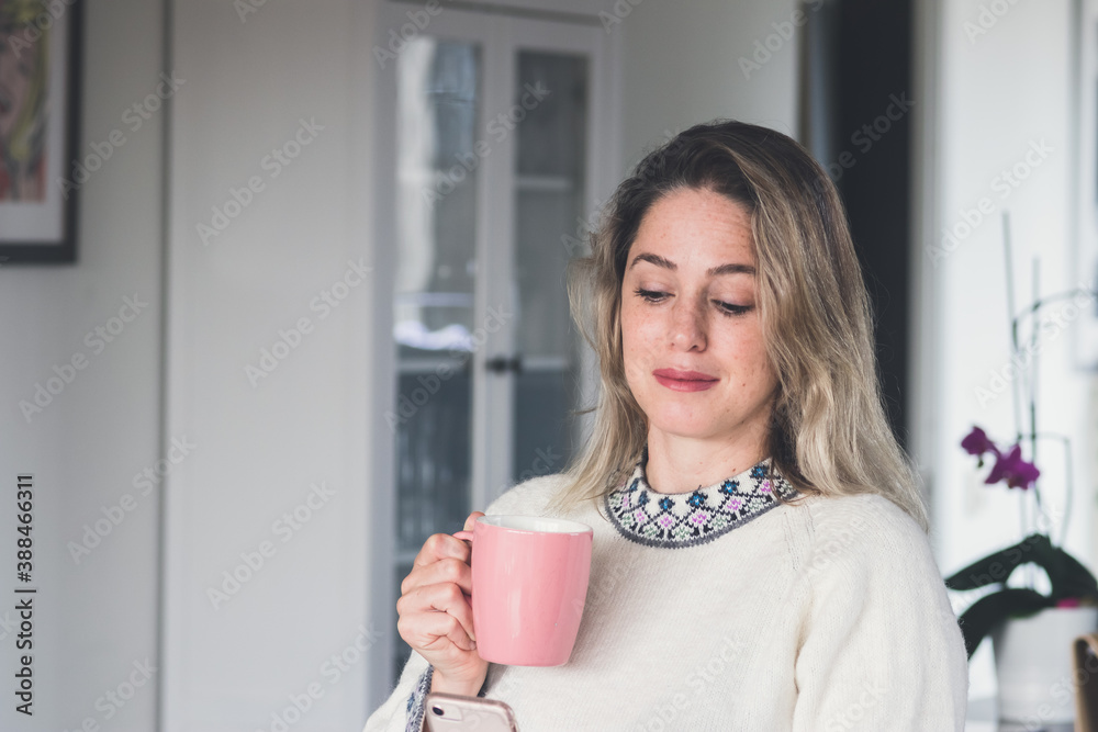 Woman drinking tea or coffee, holding a rosa and white porcelain cup , looking down at phone, dark gray background Woman drinking tea or coffee, holding a rosa and white porcelain cup , looking down at phone, dark gray background