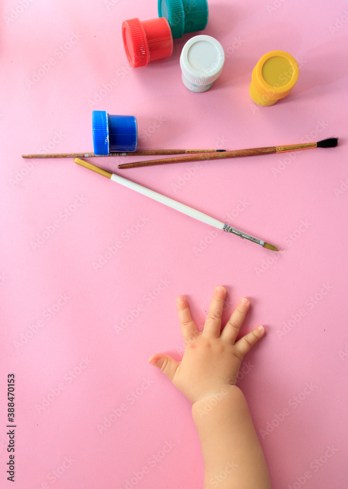a child's hand holds brushes and paints on a pink background top view with space for text a child's hand holds brushes and paints on a pink background top view with space for text