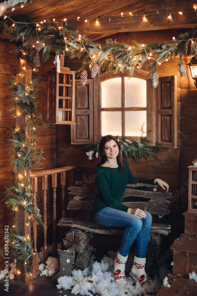young caucasian beautiful girl sits in the cozy yard of a village house decorated for the New Year