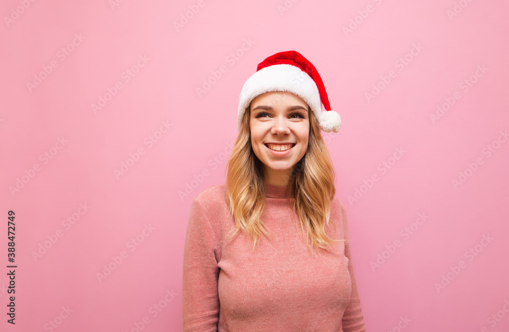 Portrait of happy girl in a santa hat on a pink background, looking away and smiling. Christmas lady in cute happy clothes isolated on pink background. Copy space Portrait of happy girl in a santa hat on a pink background, looking away and smiling. Christmas lady in cute happy clothes isolated on pink background. Copy space