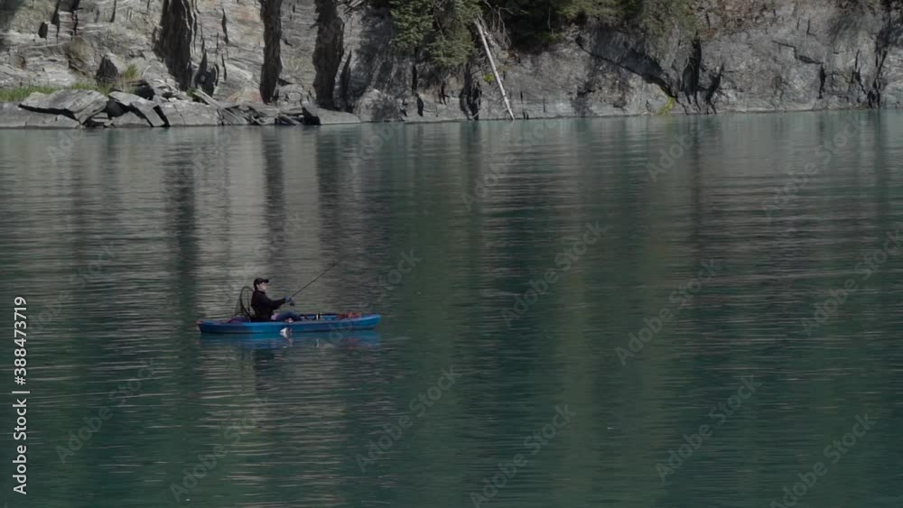 slow motion cast of fishing rod from fisher woman on kayak with the cliffside shoreline reflecting in the green ocean water. slow motion cast of fishing rod from fisher woman on kayak with the cliffside shoreline reflecting in the green ocean water.