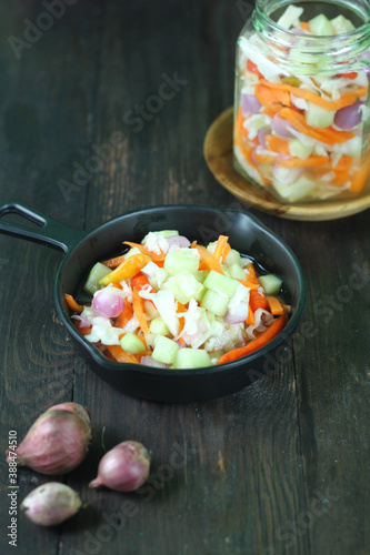 Acar timun or acar sayur ,  typical Indonesian traditional vegetables pickles made from carrot, cucumber, cabbage, shallot, and chili.  Dark wooden background. Selective focus. 