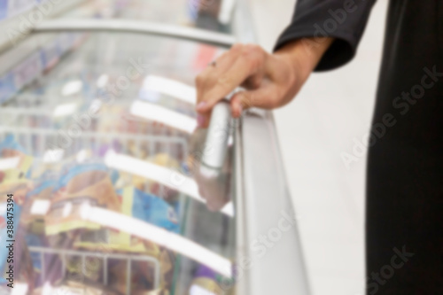 A woman opens a display case in the frozen food section. Blurred.