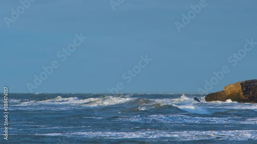 A group of people engaged in kitesurfing in sunny autumn day, high waves, Baltic Sea Karosta beach in Liepaja, medium shot