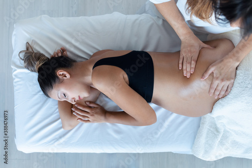 Beautiful young physiotherapist woman massaging tummy on pregnant woman on a stretcher at home.