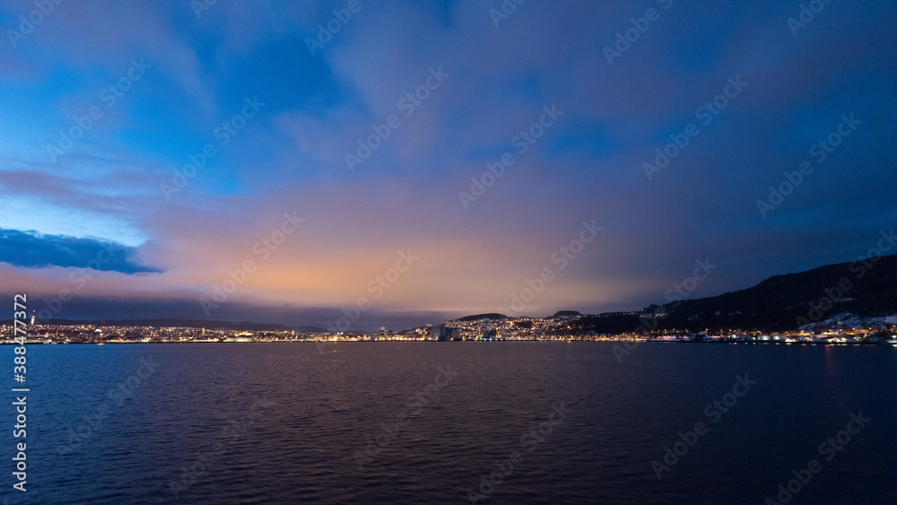 Approaching the illuminated norwegian city Trondheim in early dawn seen from the sea on cruise ship