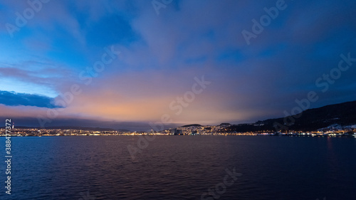 Approaching the illuminated norwegian city Trondheim in early dawn seen from the sea on cruise ship