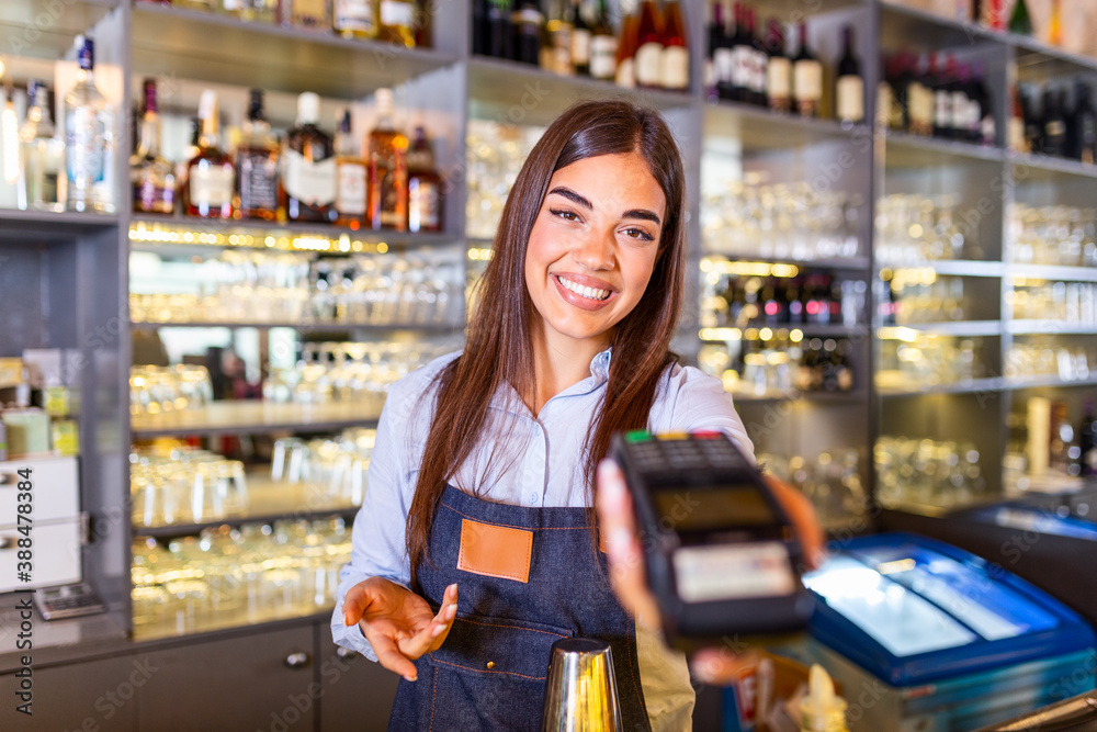 Waitress at cash counter holding an electronic card payment machine. Close up of young woman holding wireless terminal POS at coffee shop