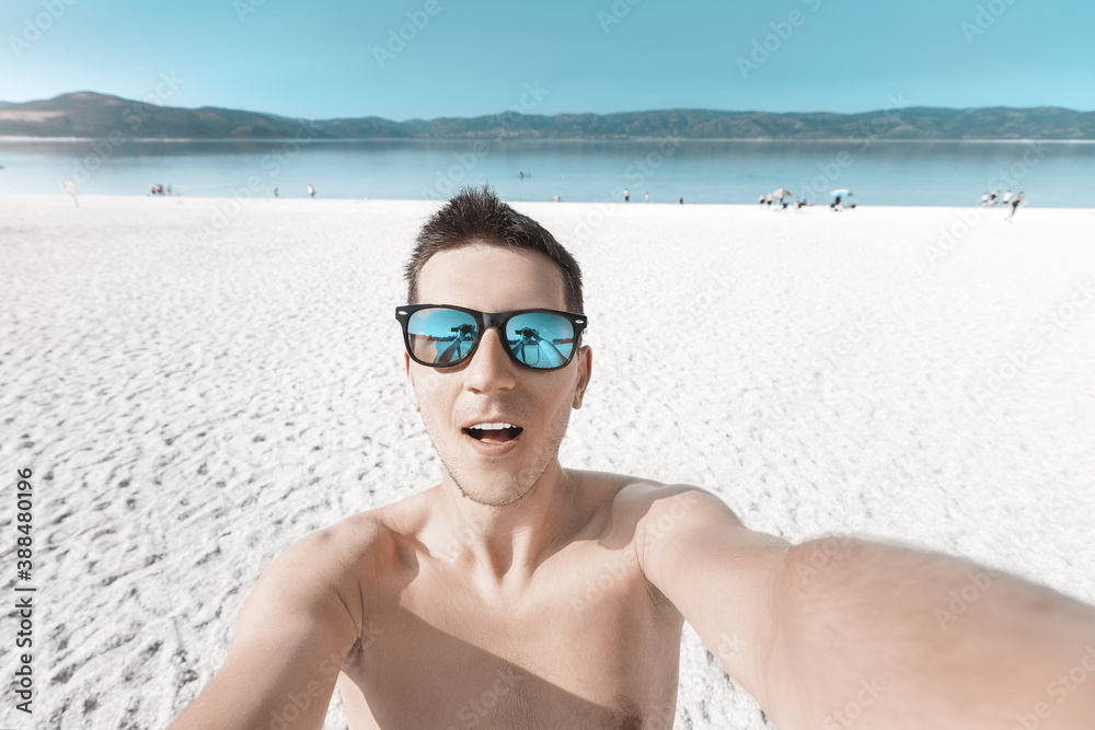 A happy young guy takes a selfie on the sea coast with bright white sand. Vacation and free lifestyle in youth concept A happy young guy takes a selfie on the sea coast with bright white sand. Vacation and free lifestyle in youth concept