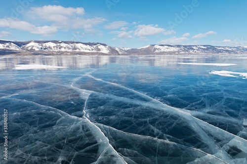 Frozen Baikal Lake on a sunny February day. Beautiful blue smooth ice with cracks in the Small Sea Strait. Poles mark the ice road to Olkhon Island. Winter ice travel. Natural background