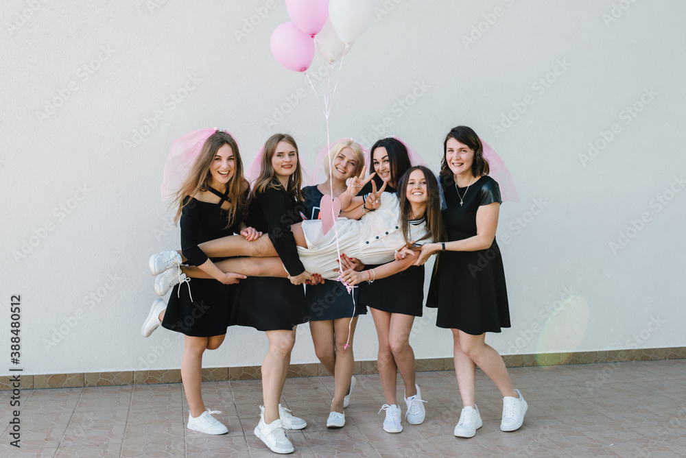 Fototapeta premium Beautiful sexy young girls hold pink air balloons in dress and veil on bachelor party. Bride hugging bridesmaids smiling outdoors and celebrating bachelorette party. Maiden evening, Hen-parties.