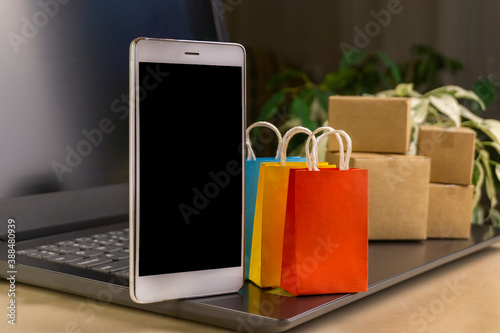 online shopping concept. little deliver boxes, smartphone, shopping bags, shopping bascket stand on laptop. copy space