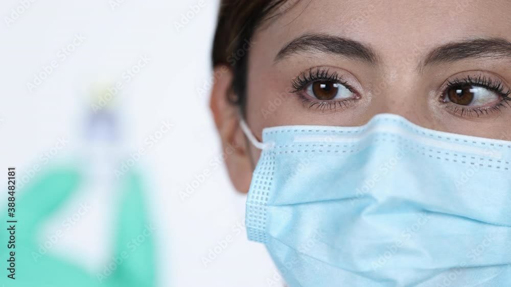 Rack focus from eyes of woman wearing mask to vaccine vial she holds in her hand. Rack focus from eyes of woman wearing mask to vaccine vial she holds in her hand.
