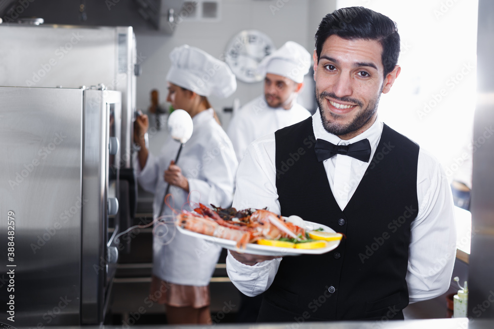 Portrait of handsome waiter with dish of seafood in kitchen on fish restaurant