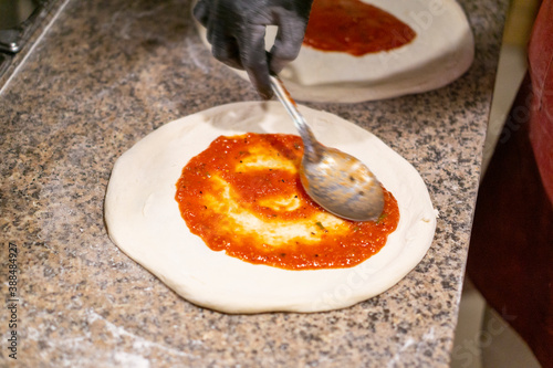 chef pizza with a metal spoon spreads tomato sauce on the dough in gloves. copy space