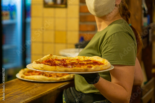 the finished pizza is picked up by a waitress in a mask and gloves from the kitchen to bring to customers. copy space
