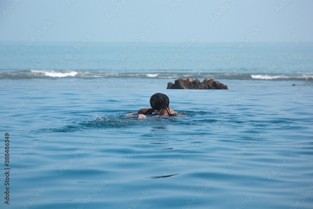 Joyful couple swimming on the infinity pool with sea view on the background, honeymoon couple swimming