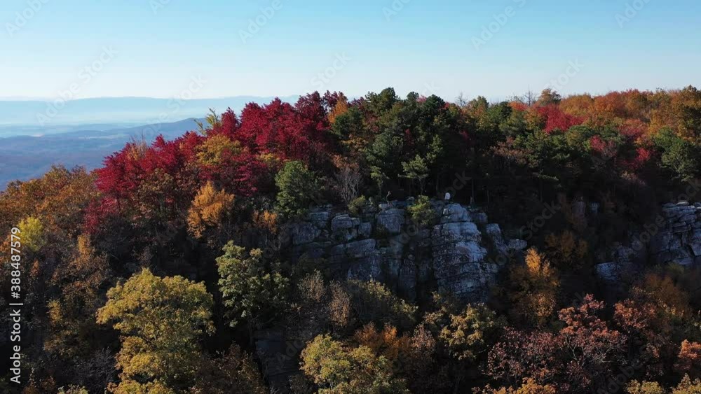An aerial shot of a man standing on Tibbet Knob, part of Great North Mountain, the border between Virginia and West Virginia. The leaves of the trees are bright with autumn colors.