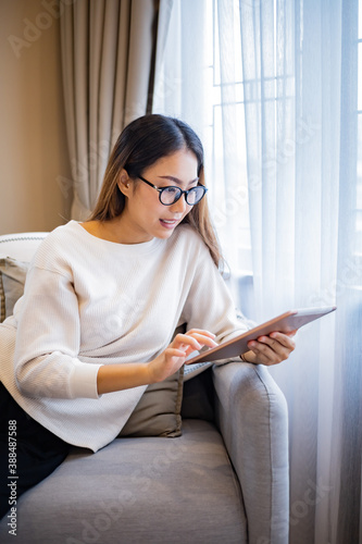 Asian woman who wear glasses relaxing on sofa while use tablet.
