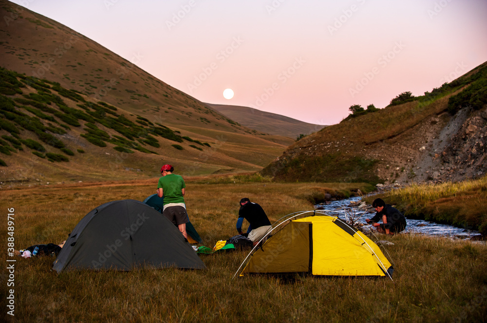 Group of trekkers camping in mountain pass. Climbers pitch tent in nature near Sary Chelek lake, Sary-Chelek Jalal Abad region, Kyrgyzstan, Trekking in Central Asia.