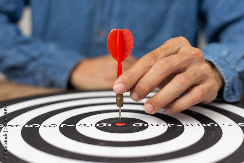 Fototapeta premium Hand Businessman holding arrow directed towards dart board target, successful business idea, A man wearing a jean shirt with a red dart Centered on the target