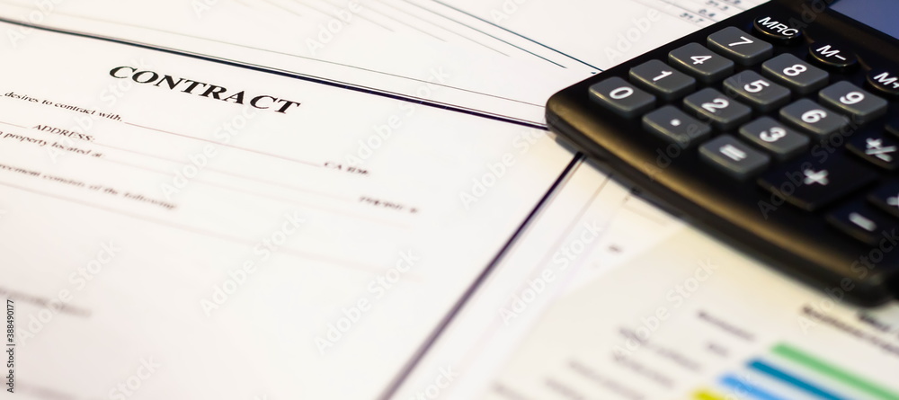 A contract document next to a calculator on a white table in the office. A contract document next to a calculator on a white table in the office.