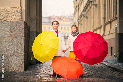 Two cheerful girls with colorful umbrellas on the street of old city in the autumn day.