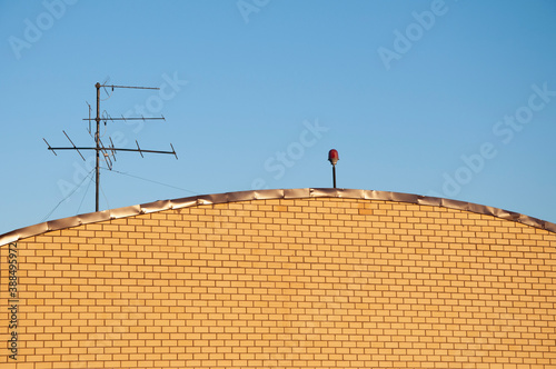 a brick wall, a television antenna and an orange lantern against a blue sky background