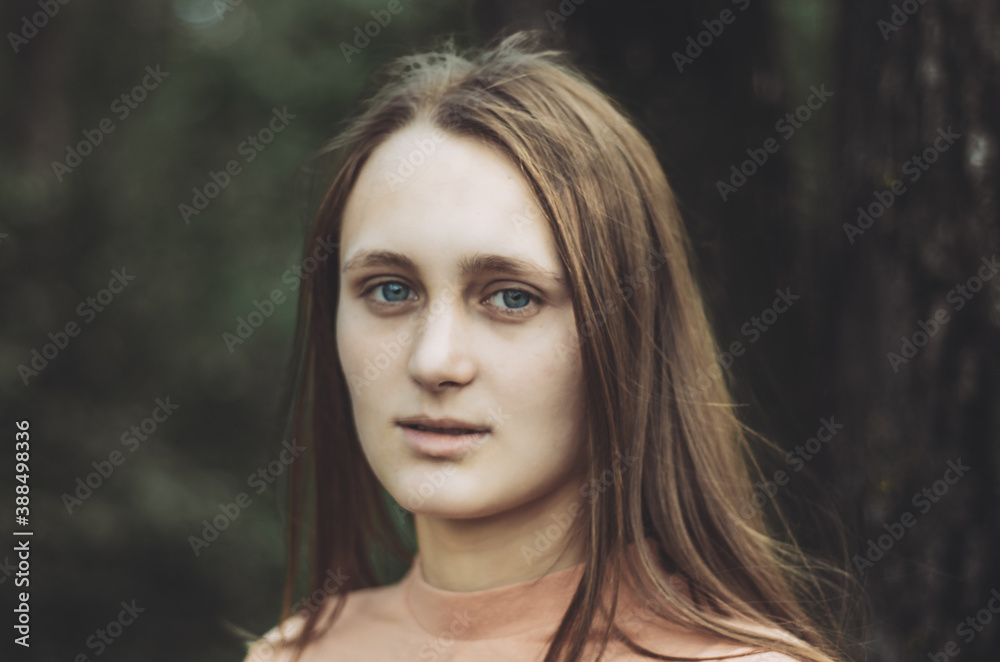 Portrait of a young woman with neutral face expression looking to the camera, with a forest background Portrait of a young woman with neutral face expression looking to the camera, with a forest background
