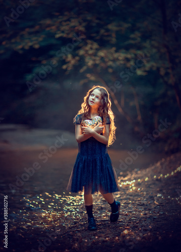 Obraz na płótnie A girl in a blue dress looking at the sky and holding a glowing heart in her hands in the night forest w salonie