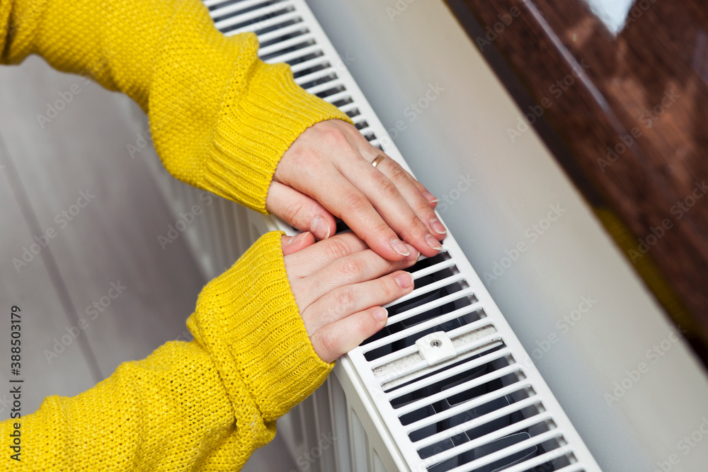 The woman warms her hands on the radiator - obrazy, fototapety, plakaty 